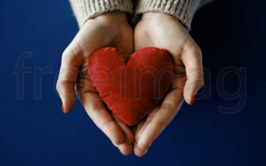Dos manos  sostienen un corazón rojo sobre un fondo azul